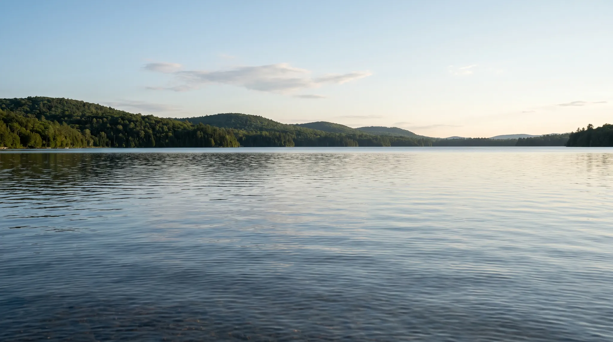A small white motorboat on a calm lake below wooded hills